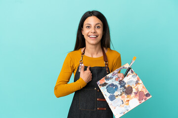 Young artist caucasian woman holding a palette isolated on blue background with surprise facial expression