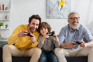 KYIV, UKRAINE - APRIL 12, 2021: Men and kid with joysticks playing video game at home © LIGHTFIELD STUDIOS