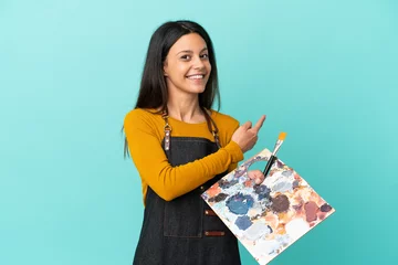 Fotobehang Young artist caucasian woman holding a palette isolated on blue background pointing back © luismolinero