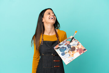 Young artist caucasian woman holding a palette isolated on blue background laughing