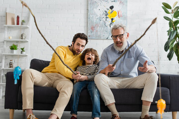 Excited boy playing fishing with father and grandfather at home