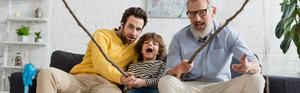 Men and excited child playing toy fishing in living room, banner