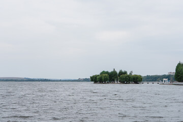 Green island among a lake on a sunny day. Island with tall trees on the river on a warm summer day.