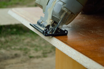 electric hand jigsaw at work, flying wooden dust and small filings
