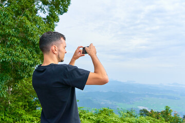 Fototapeta na wymiar The guy takes pictures on the phone of an incredible view of the mountain jungle from a high viewpoint
