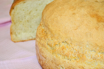 close-up - round wheat homemade bread on the background of a cut piece of bread on a pink tablecloth