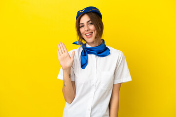 Airplane stewardess woman isolated on yellow background saluting with hand with happy expression