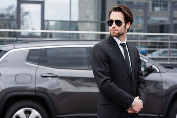 businessman in suit and sunglasses standing near modern car