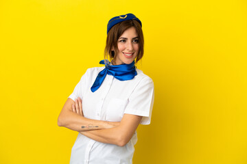 Airplane stewardess woman isolated on yellow background with arms crossed and happy