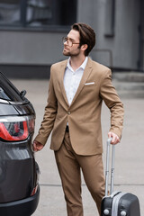 Obraz premium man in suit and glasses standing with suitcase near modern car