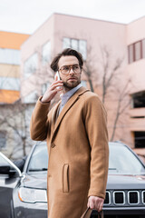 young man in glasses and coat talking on smartphone outside