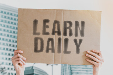The phrase " Learn daily " on a banner in men's hand. Human holds a cardboard with an inscription. Business. Education. Process. Improvement. Brain. Knowledge. Course. Couching
