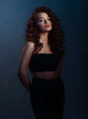 Naklejka premium Beauty young woman with curly big and long hair. Glamour lady on dark blue background. Cute woman face wavy hair, perfect make up, red lips