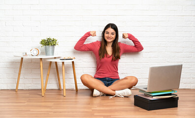 Young woman with a laptop sitting on the floor at indoors doing strong gesture