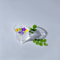 Flower juice. Flowers in a glass of water. Shadow of a glass. On a gray background. Minimal composition.