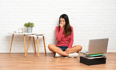 Young woman with a laptop sitting on the floor at indoors having doubts