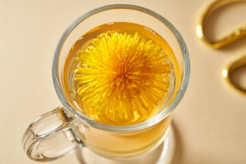 A cup of dandelion tea with fresh dandelion flowers on a beige background