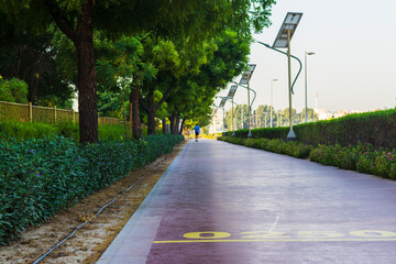 Middle aged man walking on jogging track in Nad Al Hamar park, early in the morning. Lamp post powered by solar panels can be seen in the picture. Outdoors