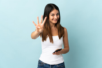 Young caucasian woman using mobile phone isolated on blue background happy and counting four with fingers