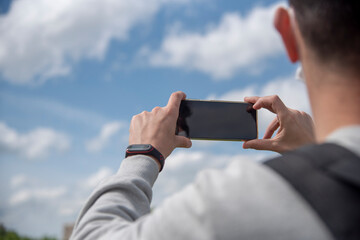 vista de un hombre sacando una foto con un móvil con el cielo de fondo y una pulsera de actividad