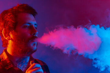 Studio portrait with colored lights of person with tattoos vaping and exhaling large amount of...