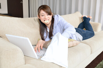 パソコンを見ながら寝転んでスナック菓子を食べる若い女性