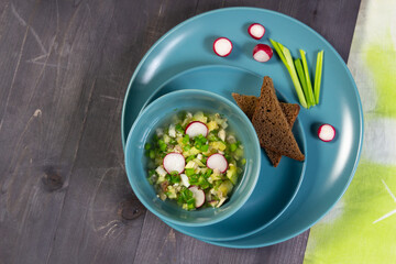 Okroshka,russian cold soup with meat, vegetables, kvass, sour cream, mustard, horseradish in blue bowl with bread  on black background