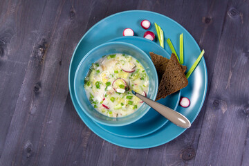 Okroshka,russian cold soup with meat, vegetables, kvass, sour cream, mustard, horseradish in blue bowl with bread  on black background