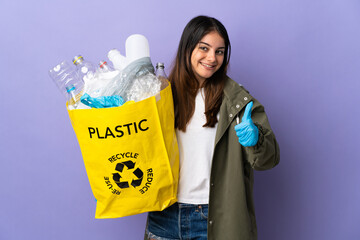 Young woman holding a bag full of plastic bottles to recycle isolated on purple background giving a thumbs up gesture