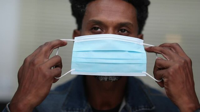 African descent man putting covid-19 face mask looking to camera