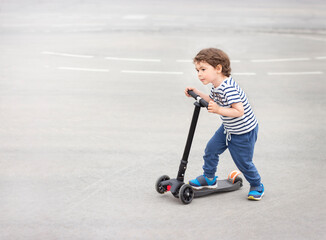 little boy in a striped T-shirt rides a scooter on the asphalt. Side view © Алена Ягупа
