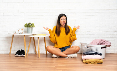 Young woman sitting on the floor at indoors with clothes basket with shocked facial expression