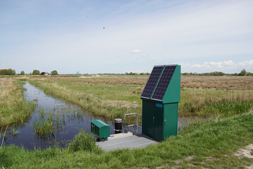Very small Dutch weir (Dutch: valve weir) with solar panels near a ditch. The weir regulates the water drainage capacity of the surface water body. Spring, meadows, May. Netherlands - obrazy, fototapety, plakaty