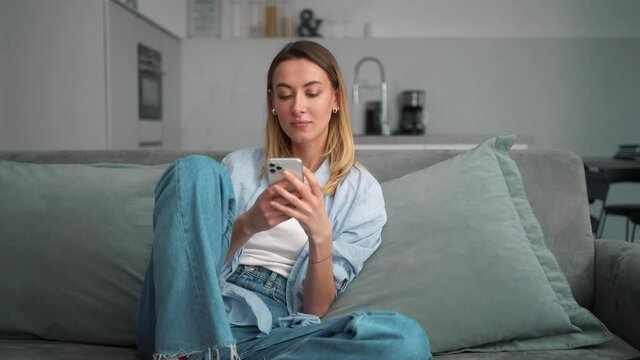 The smiling woman search something on the phone while sitting on the couch in the room