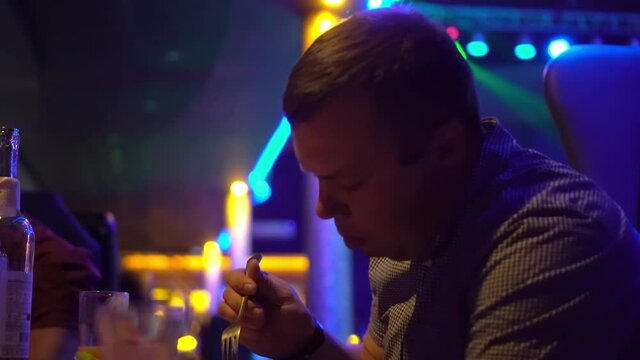 A young guy in a nightclub has a snack and drinks. He's having a great time, with the disco lights all around.
