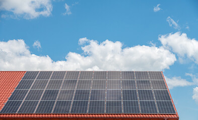 Fototapeta premium The roof of the house with solar panels against the blue sky.