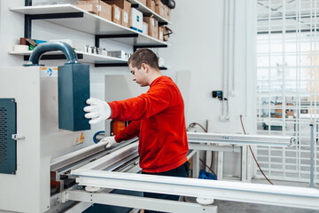 Young male worker assembling products in modern PVC and aluminum doors and windows production...