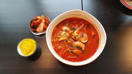 Korean food, also known as budaejigae, is served with a side dish, pickled radish and kimchi.