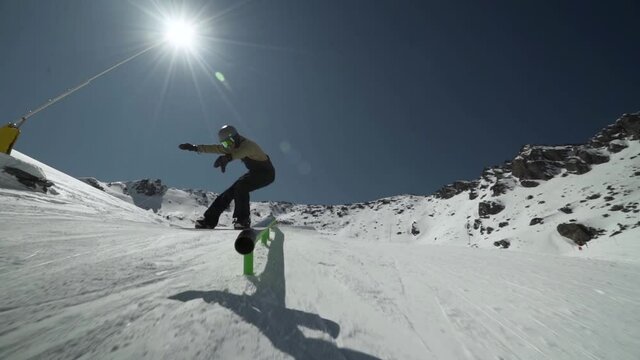 Snowboarder sliding along big steal rail performing a board lip slide during a bright sunny day in New Zealand.