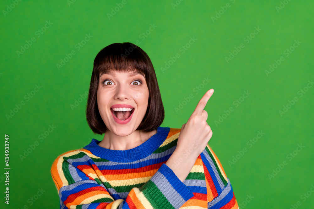 Wall mural Photo of cheerful amazed young happy woman point finger empty space sale news isolated on green color background