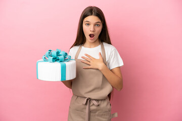 Little girl with a big cake over isolated pink background surprised and shocked while looking right