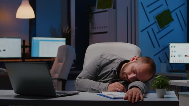 Exhausted overworked businessman sleeping on desk table in startup business office after analysing financial statistics late at night. Workaholic tired manager working at economic deadline project