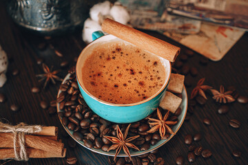 Cup of black hot coffee with foam close up on background coffee beans, anise, cinnamon sticks and cotton on a wooden table, lifestyle and coffee concept 