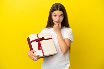 Little girl holding a gift over isolated yellow background thinking