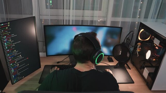 A back view of a man gamer wearing headphones is streaming online videogames on professional powerful computer sitting at home