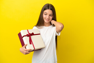 Little girl holding a gift over isolated yellow background laughing