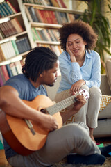 A young man plays the guitar for his wife at home. Family, together, love, music