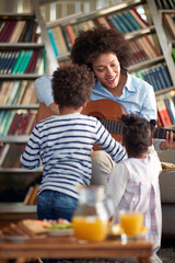 Fototapeta na wymiar Young Mom sings and plays the guitar for her children at home. Family, together, love, playtime