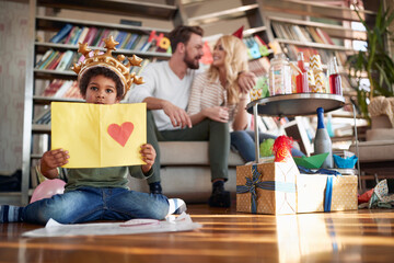 An adopted little boy sitting on the floor and posing for a photo at a kids birthday party at home with his family. Family, celebration, together