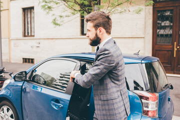 Young contemporary bearded businessman entering car going to work